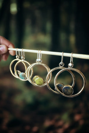 three pair of Wood and raw brass hoop earrings hanging from a stick.